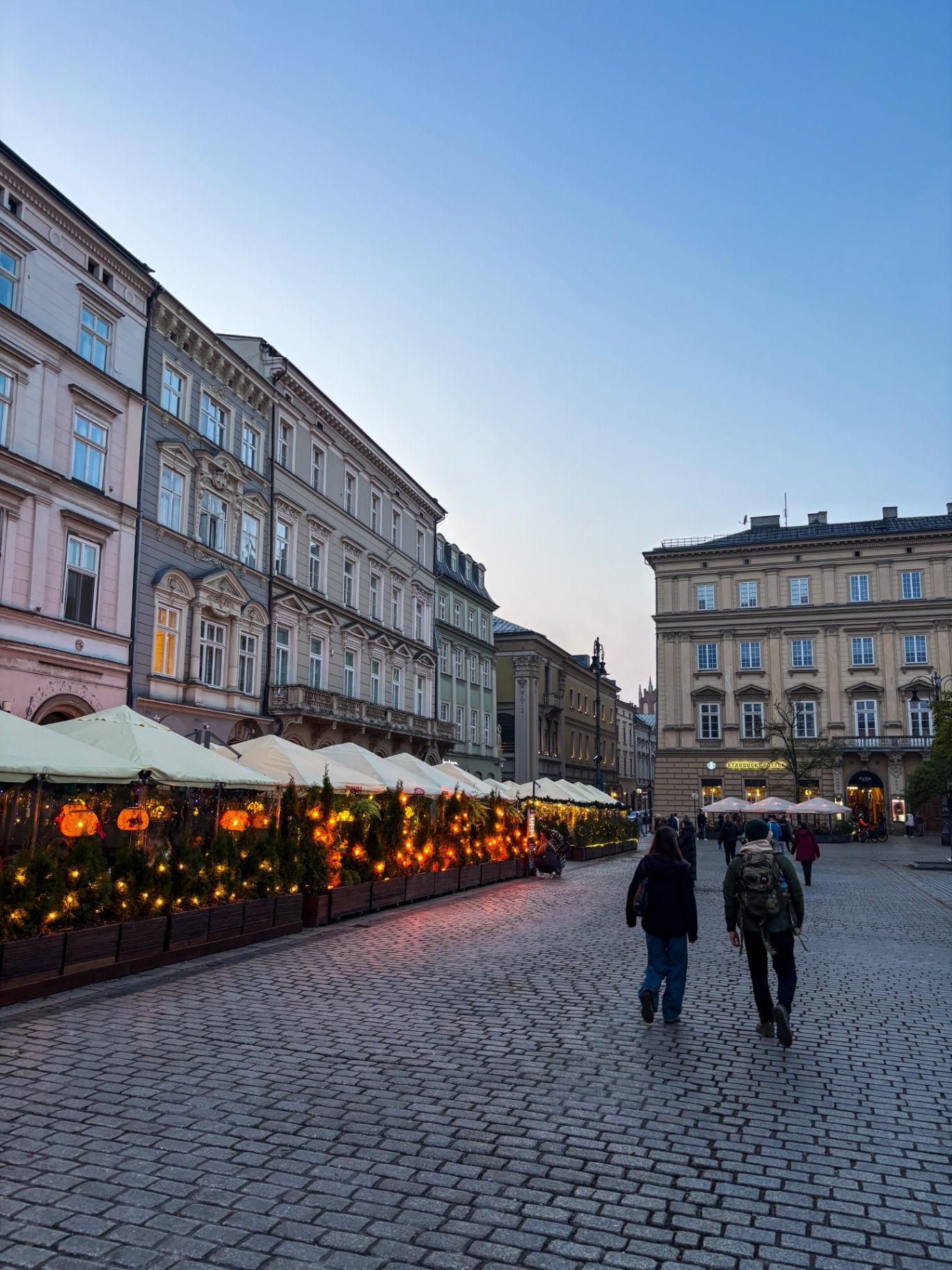 Terrasses illuminées du Rynek Glowny à Cracovie au crépuscule