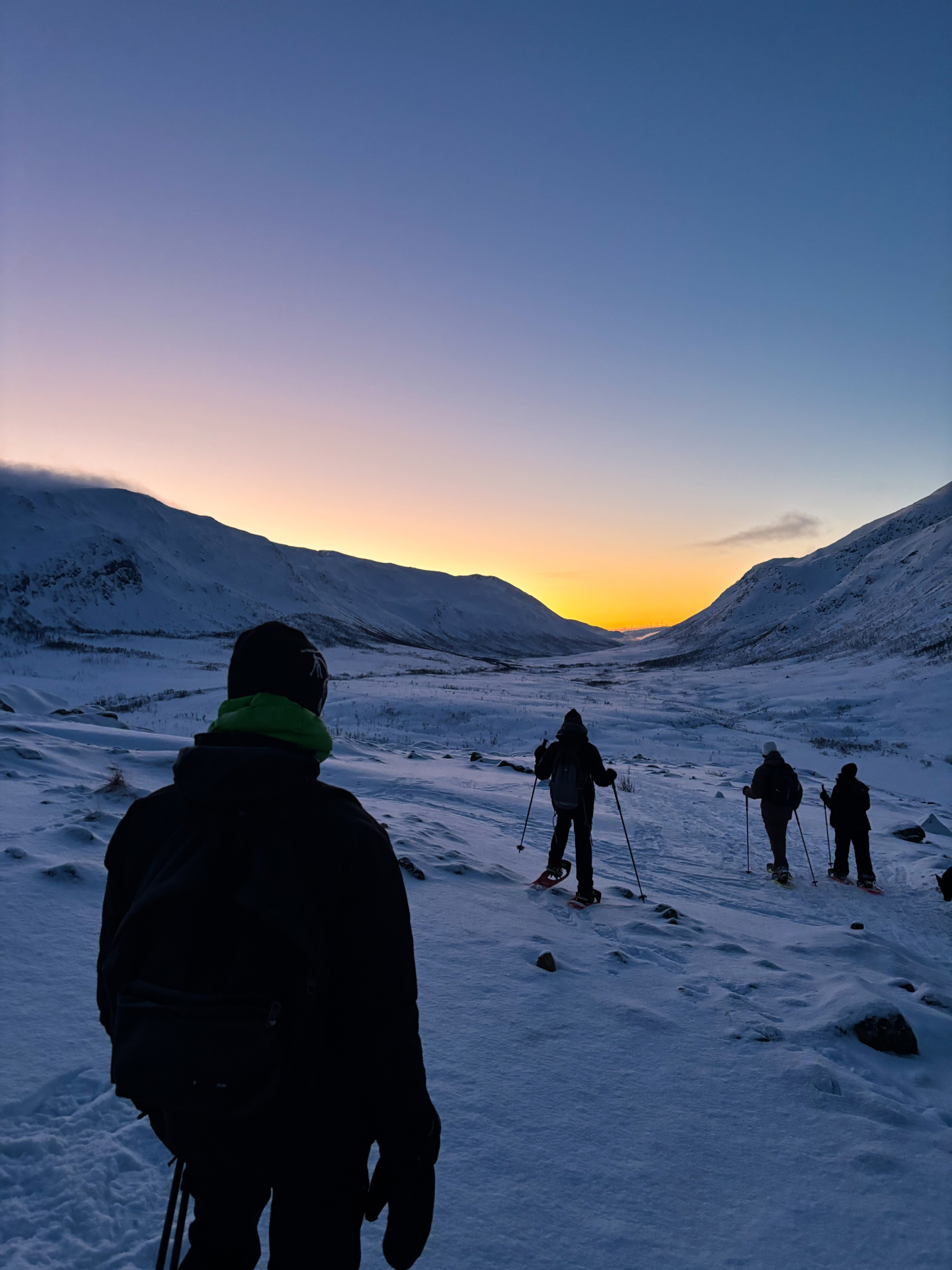 Groupe de randonneurs en raquettes marchant vers le coucher de soleil sur Kvaløya