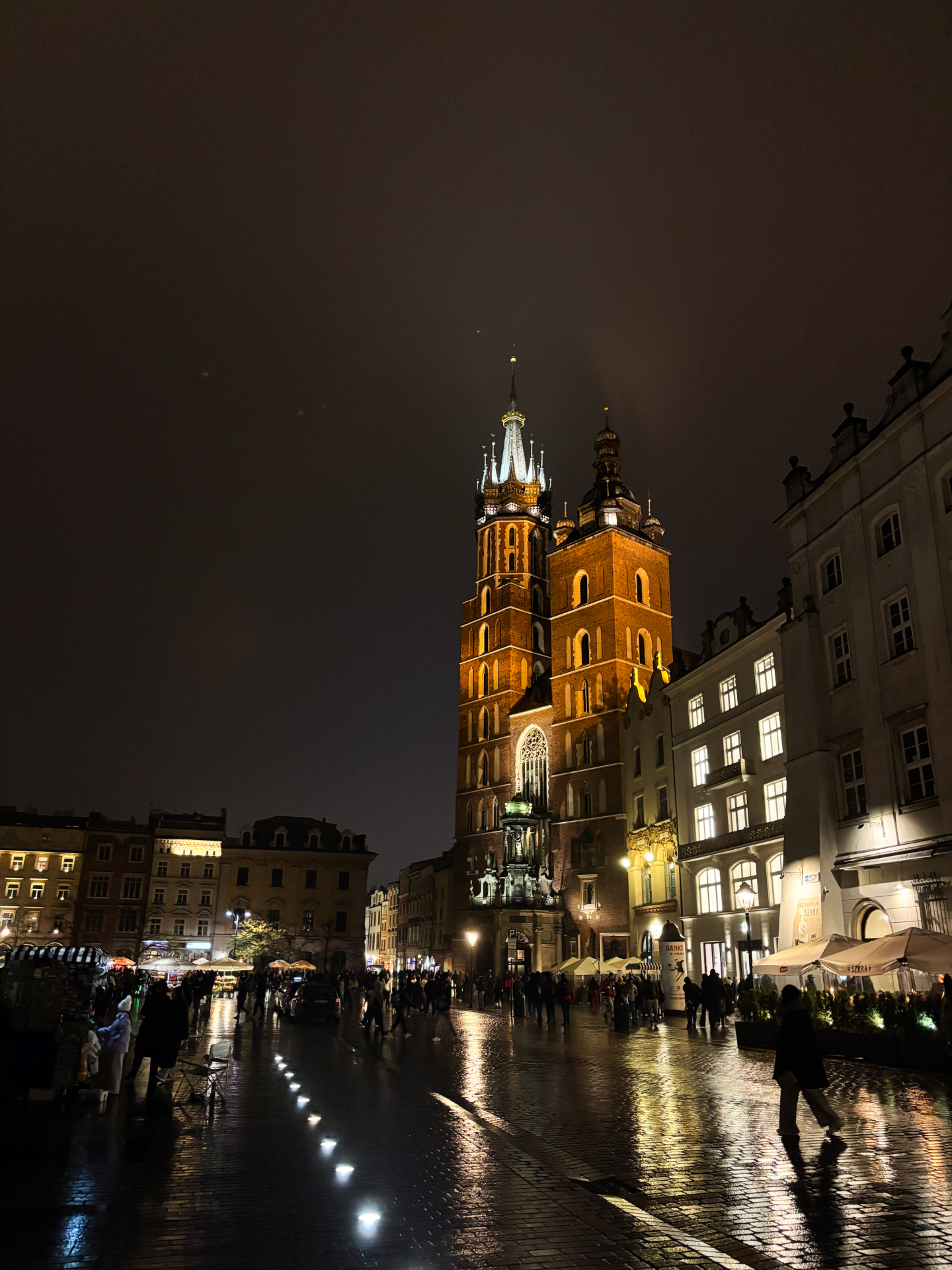 Basilique Sainte-Marie illuminée de nuit sur le Rynek Glowny, pavés mouillés par la pluie