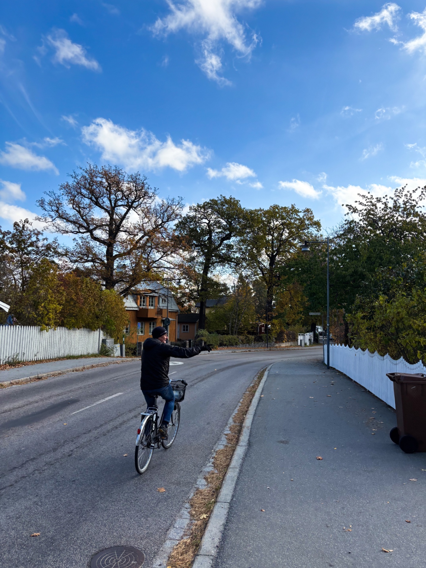 Cycliste dans une rue bordée de maisons de bois orangées et de clôtures blanches, à Saltsjöbaden