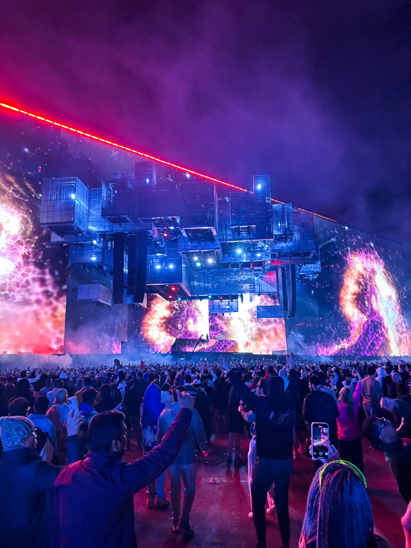 La foule du festival Soundstorm face à la structure lumineuse de la scène, écrans cosmiques de feu et rayon rouge au-dessus