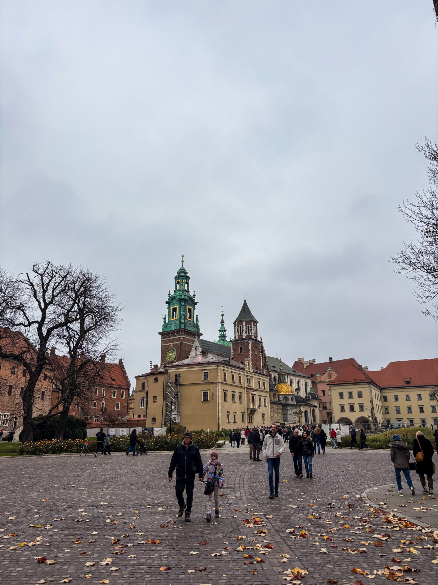 Cathédrale du Wawel avec sa tour verte sous un ciel d'automne, feuilles mortes sur les pavés