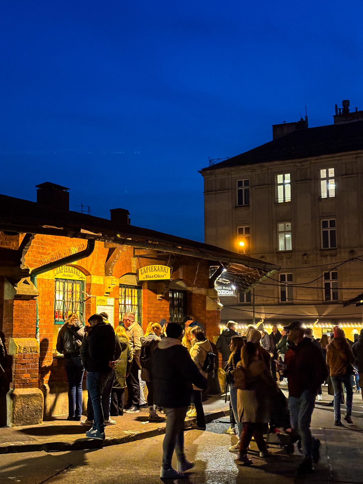 Étal de zapiekanki éclairé en pleine nuit sur la place Nowy, dans la foule de Kazimierz