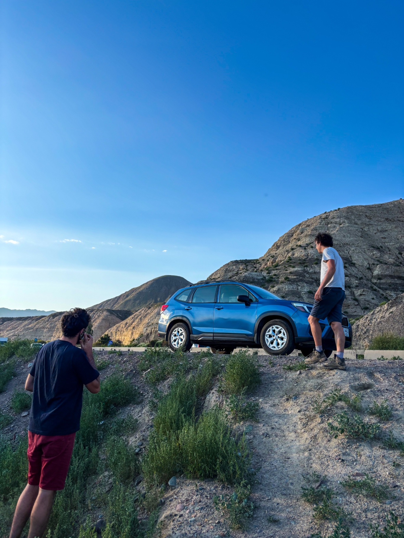 Deux voyageurs près de leur voiture bleue en surplomb de la route