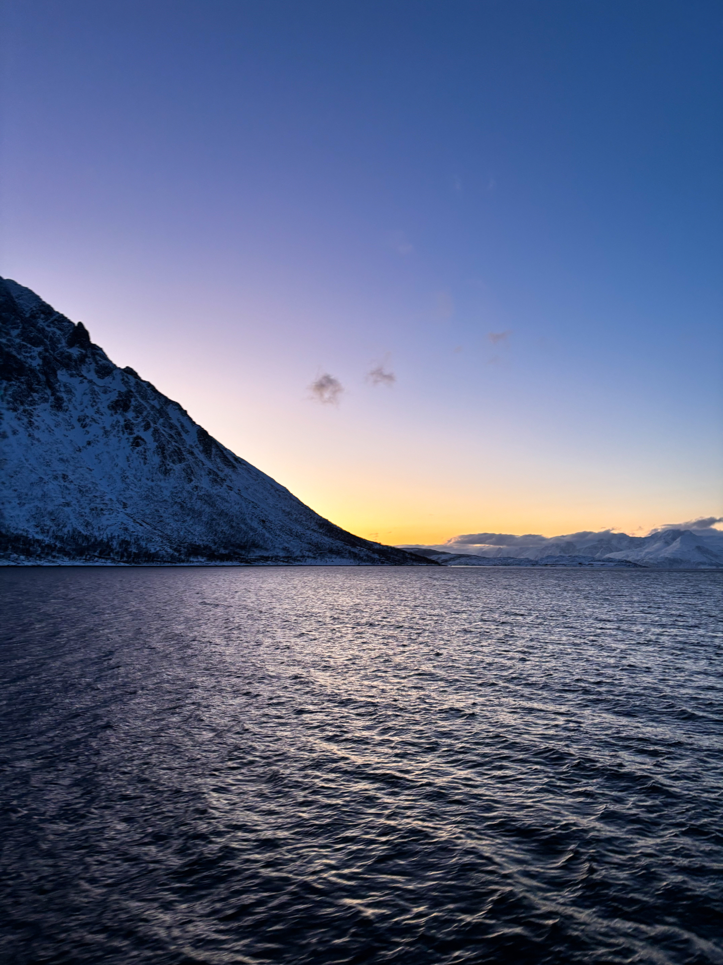 Coucher de soleil arctique sur le fjord, montagnes enneigées plongeant dans l’eau sombre