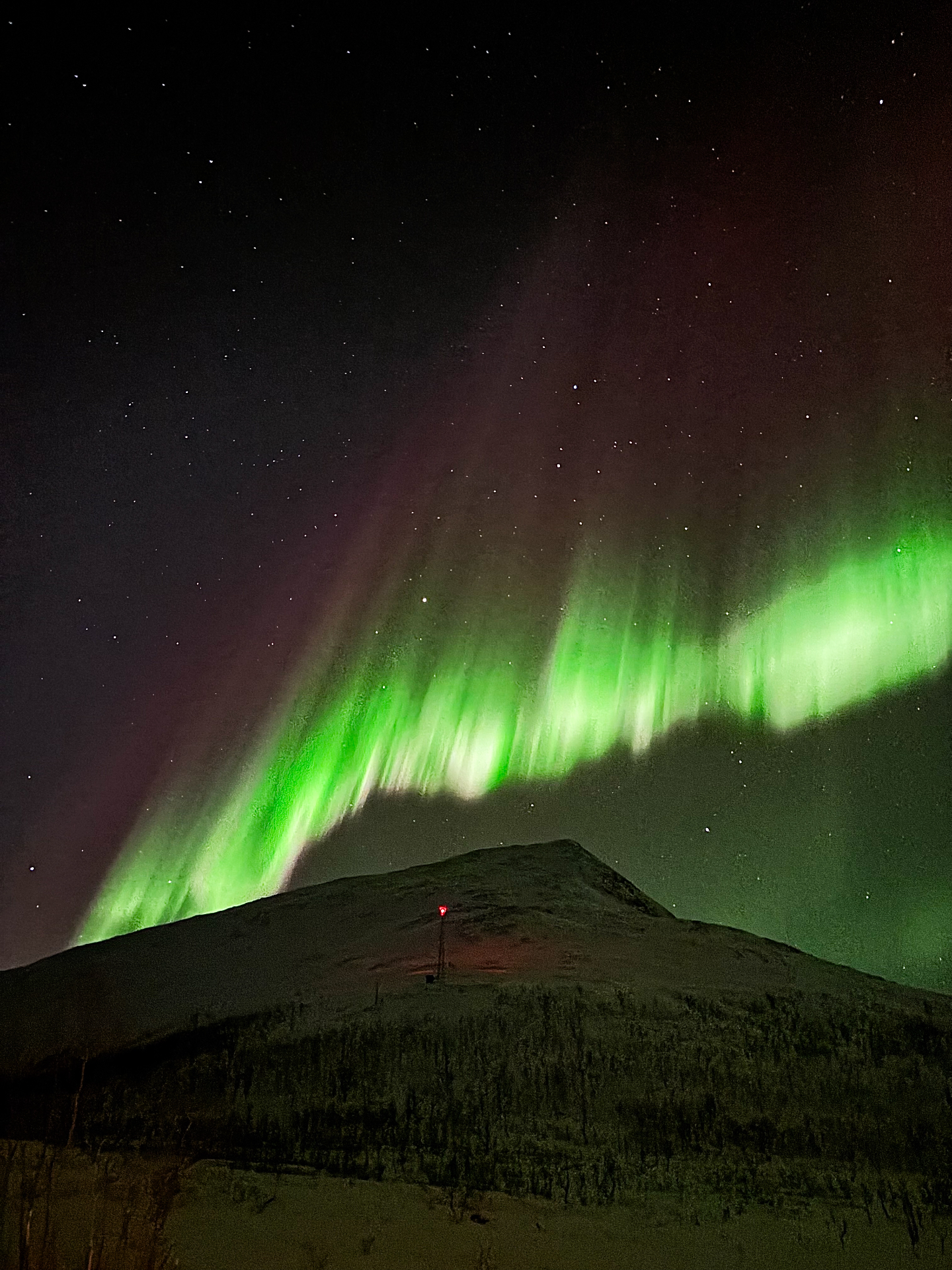 Aurore boréale verte en arc au-dessus d’une montagne enneigée près de Kvaløya