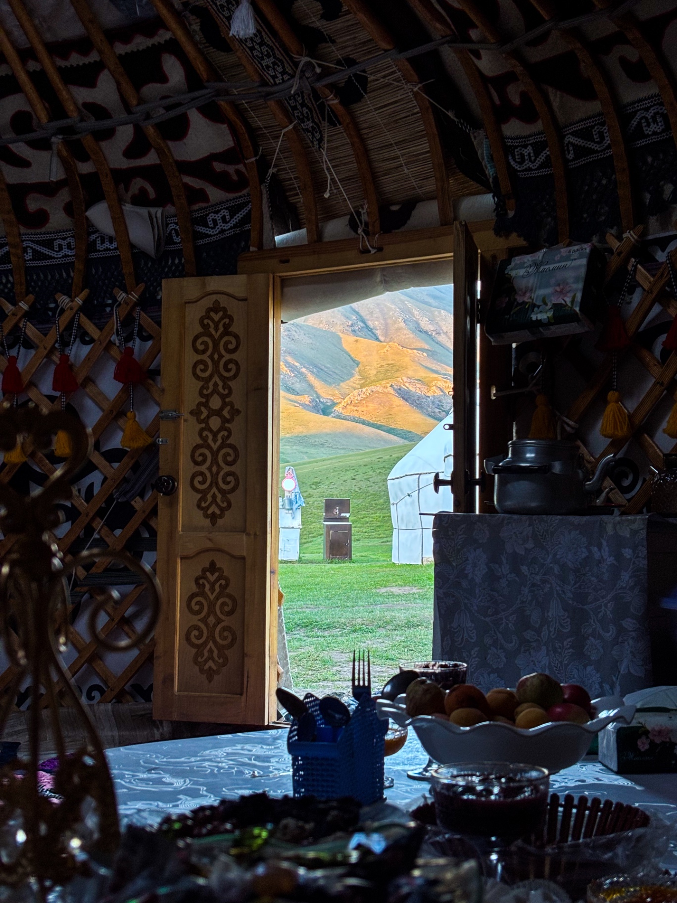 Intérieur d’une yourte kirghize avec table dressée et porte ouverte sur la vallée
