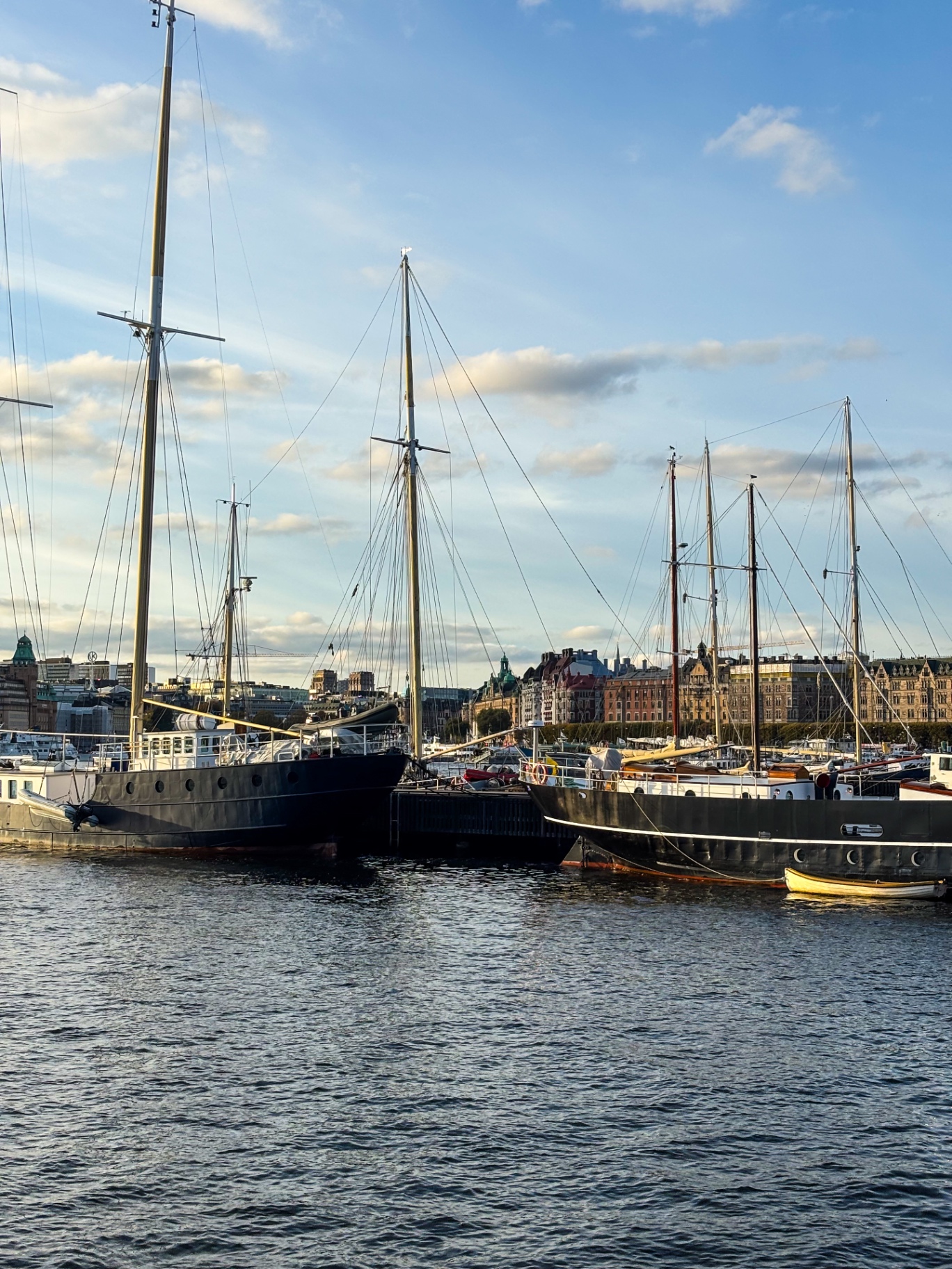 Grands voiliers traditionnels amarrés au quai face aux façades de Stockholm, dans la lumière du soir