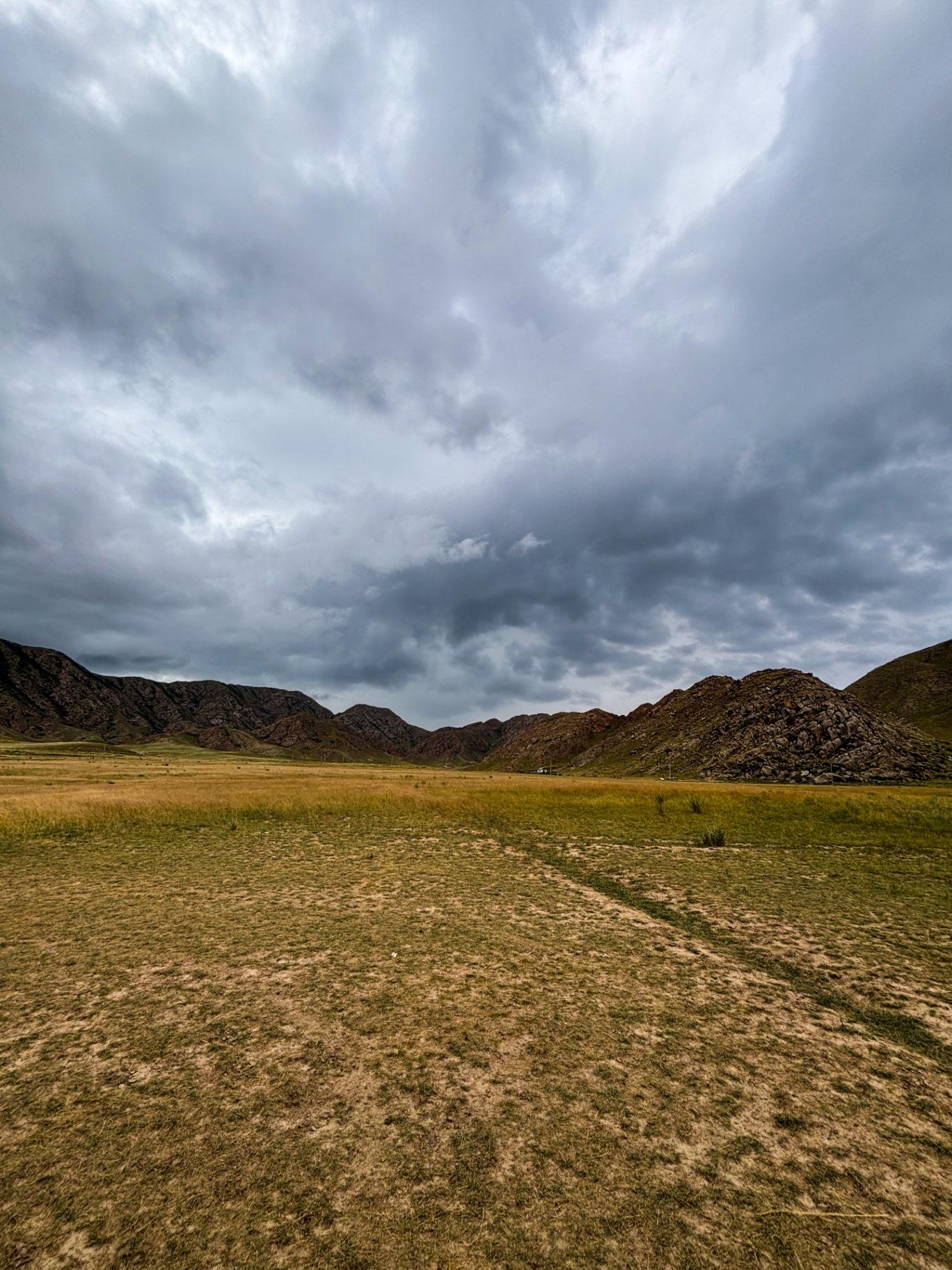 Vaste plaine dorée cernée de montagnes sous un ciel d’orage