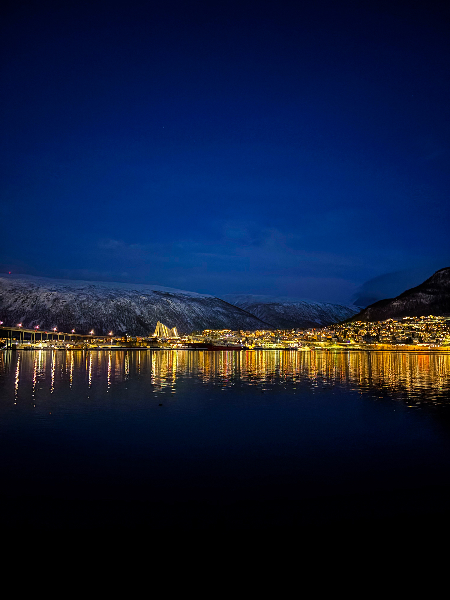 Panorama nocturne de Tromsø avec la cathédrale arctique illuminée et les lumières reflétées dans le fjord