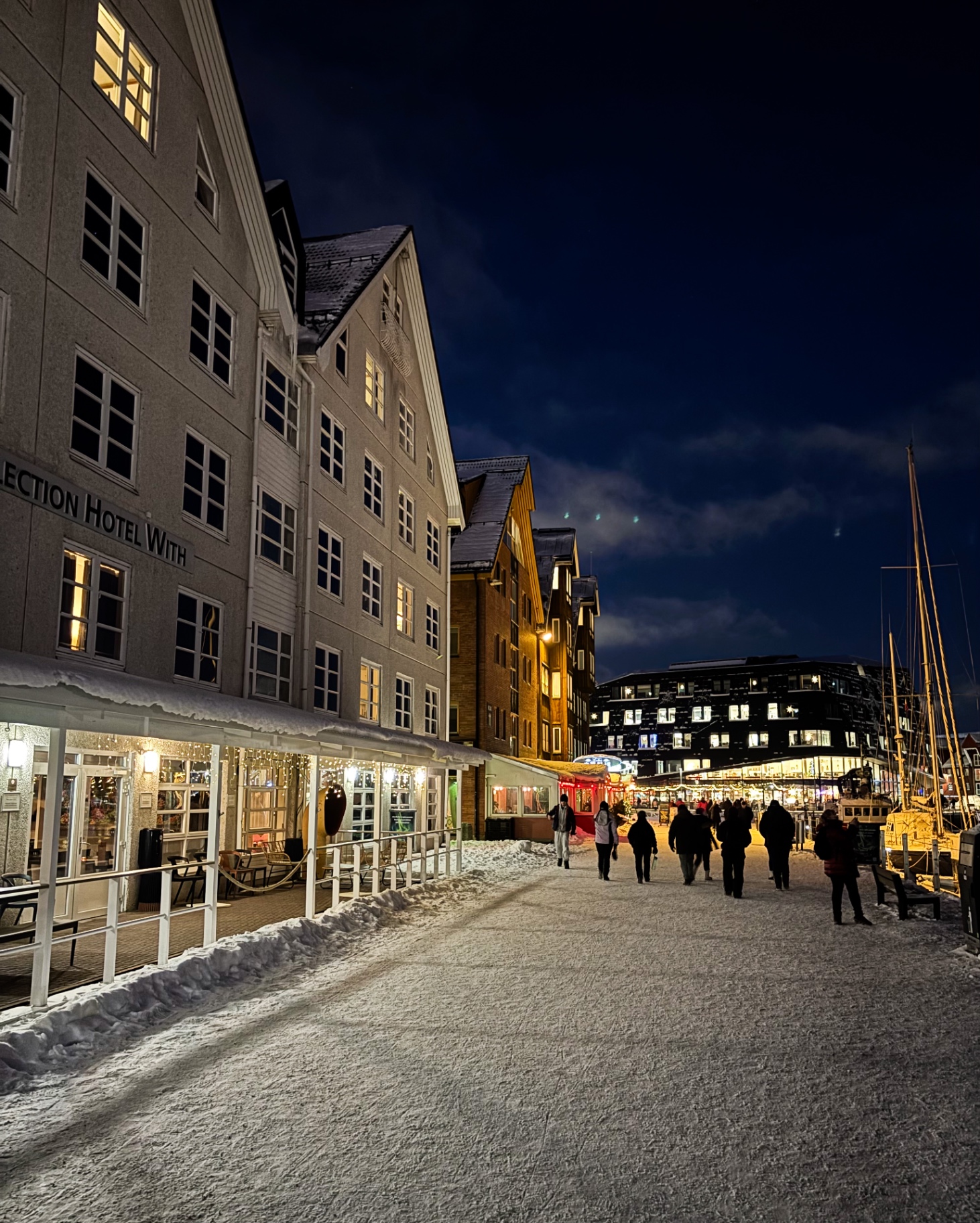 Quais de Tromsø la nuit avec façades d’hôtels, passants et neige