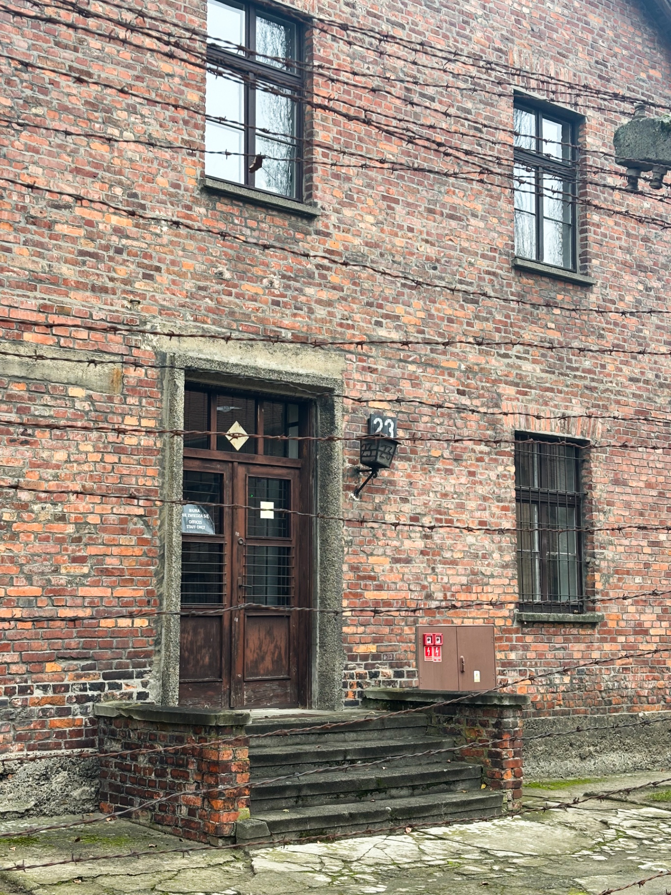 Bâtiment en briques rouges du bloc 23 derrière des fils de fer barbelés