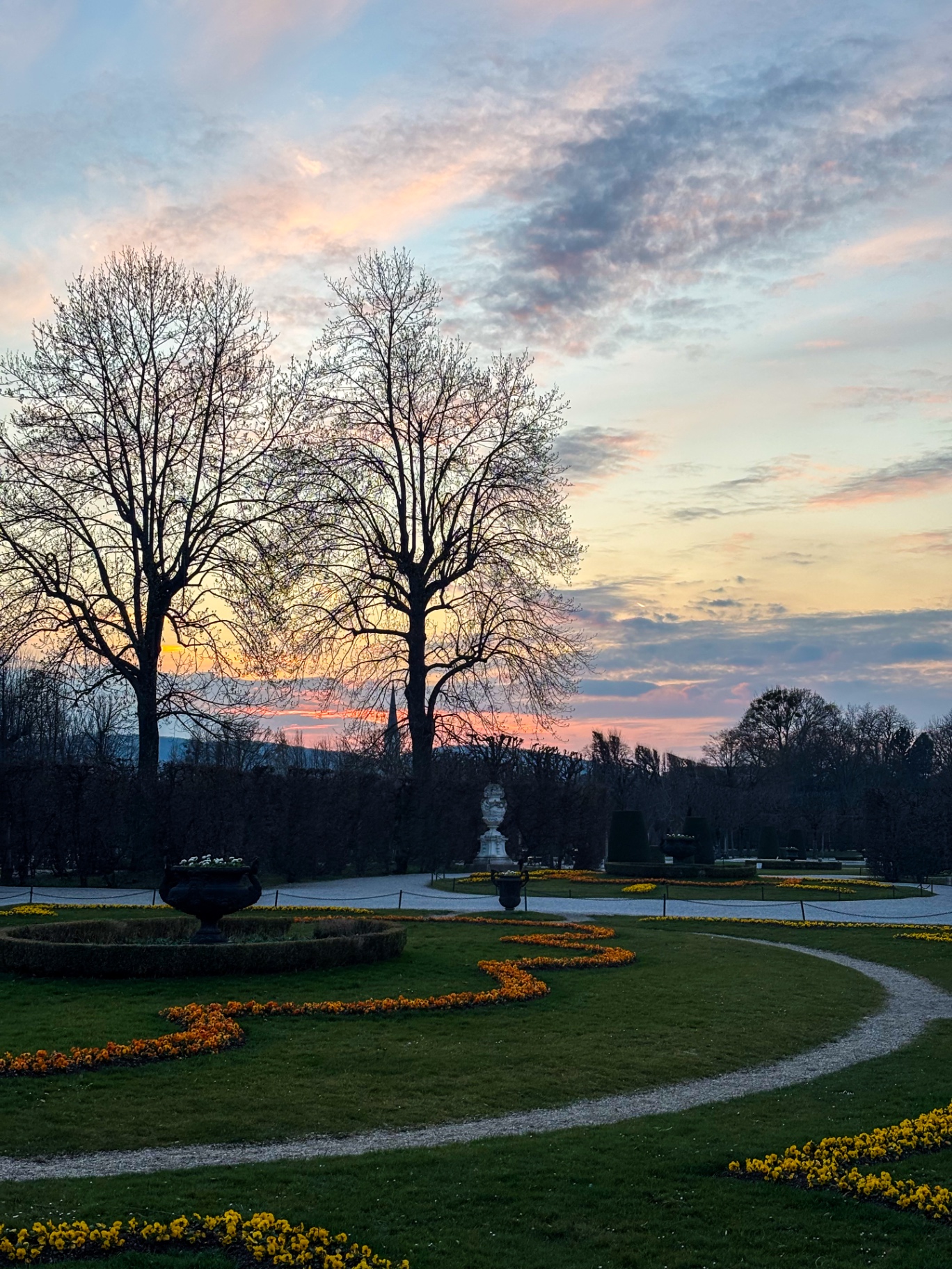 Parterres fleuris et allées des jardins de Schönbrunn au coucher du soleil, ciel doré et rose