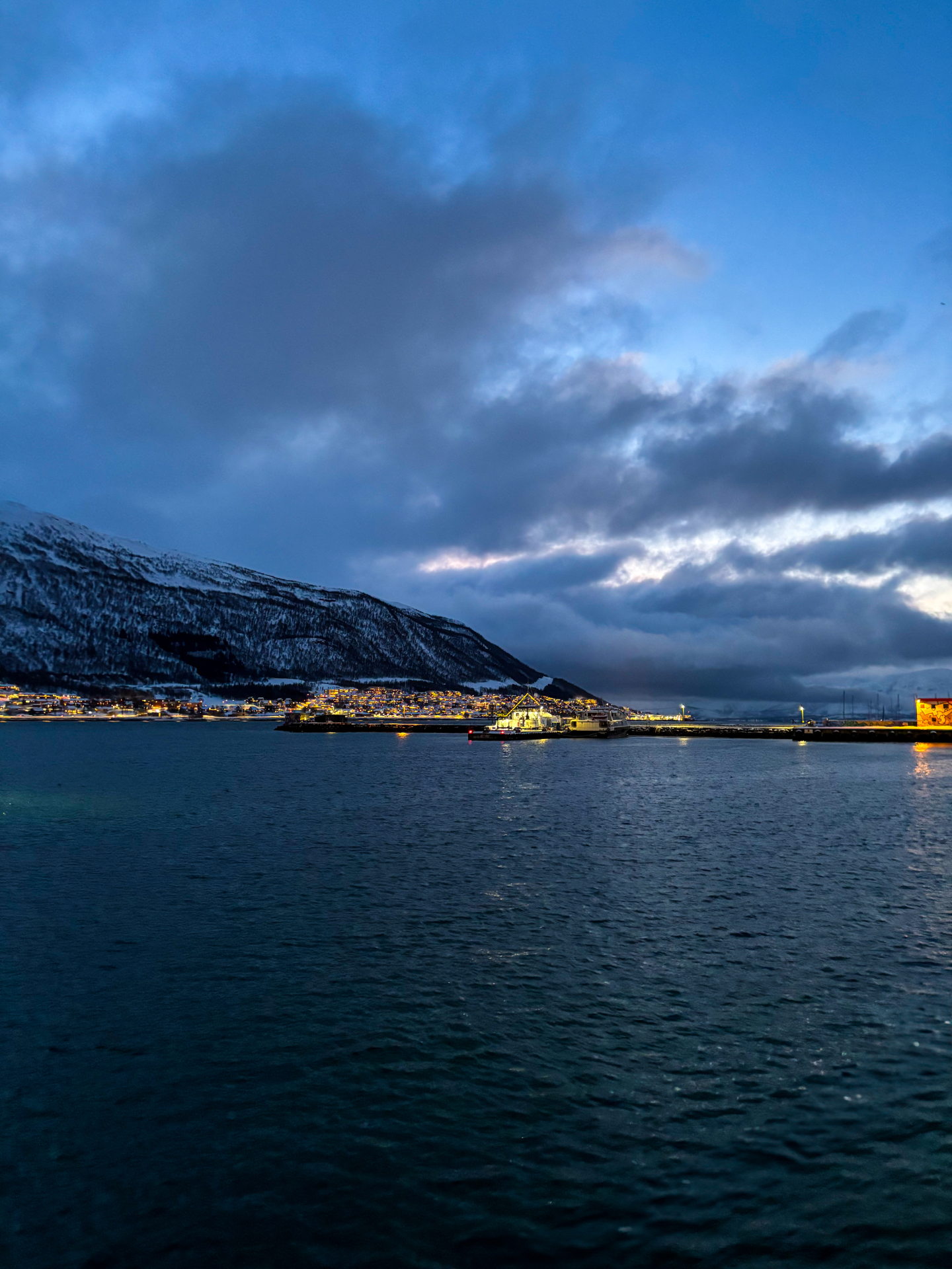 Fjord de Tromsø au crépuscule avec montagnes enneigées et lumières de la ville