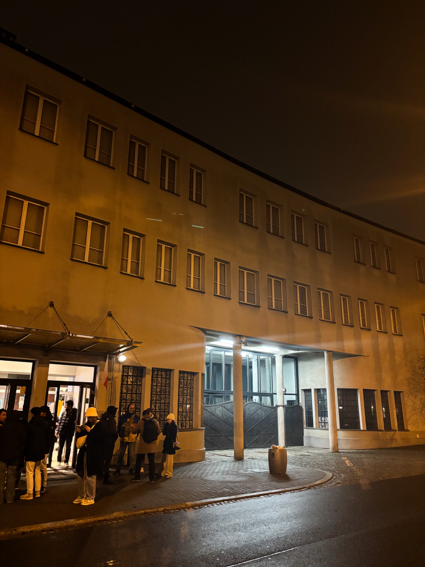 Façade de l'usine Schindler éclairée à la tombée de la nuit, visiteurs rassemblés à l'entrée