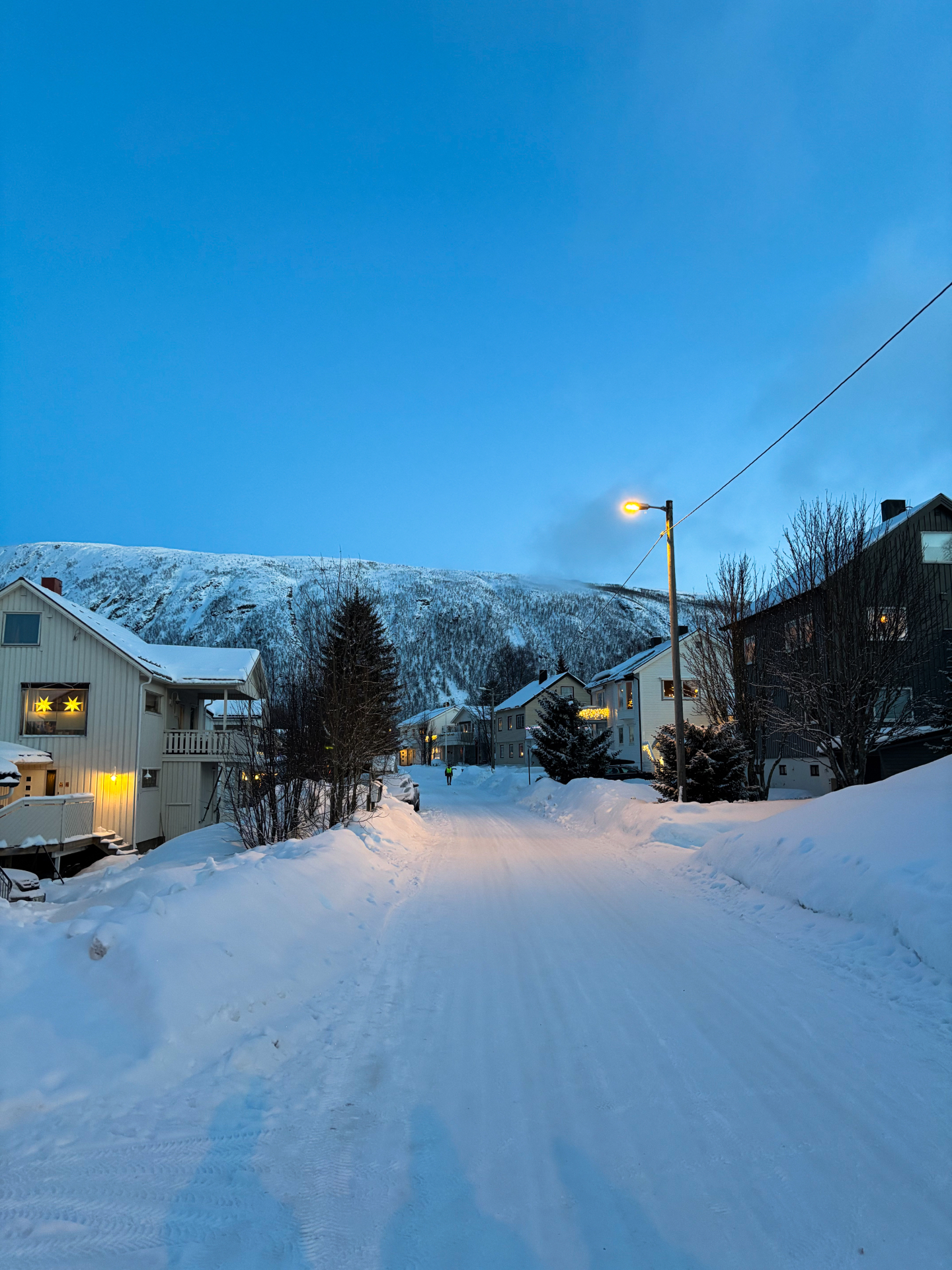 Rue enneigée de Tromsdalen au crépuscule bleu, maisons et montagnes en arrière-plan