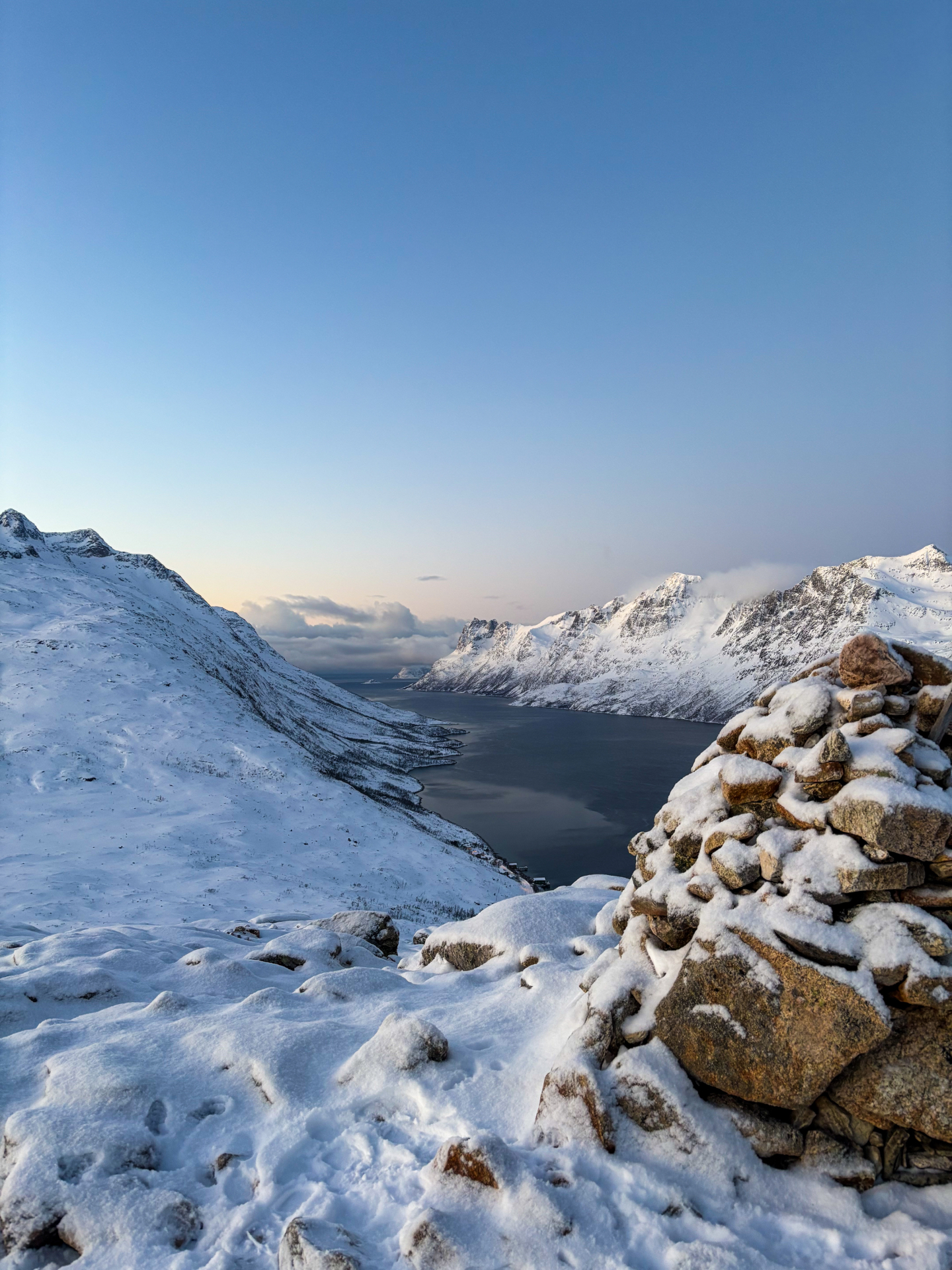 Cairn et fjord enneigé depuis le sommet de la randonnée sur Kvaløya