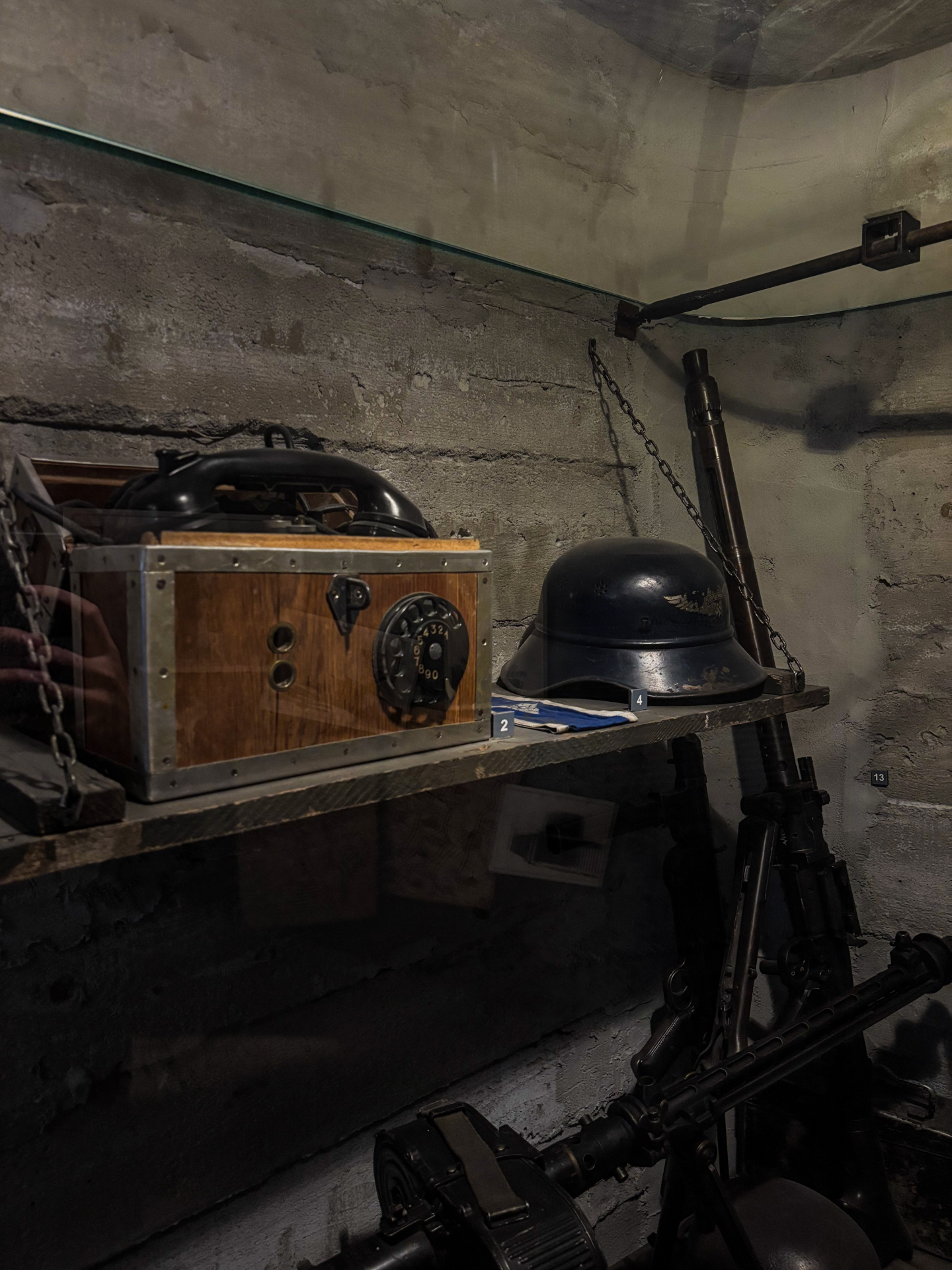 Vitrine d'armes du musée : téléphone de campagne, casque allemand et mitrailleuses derrière une vitre