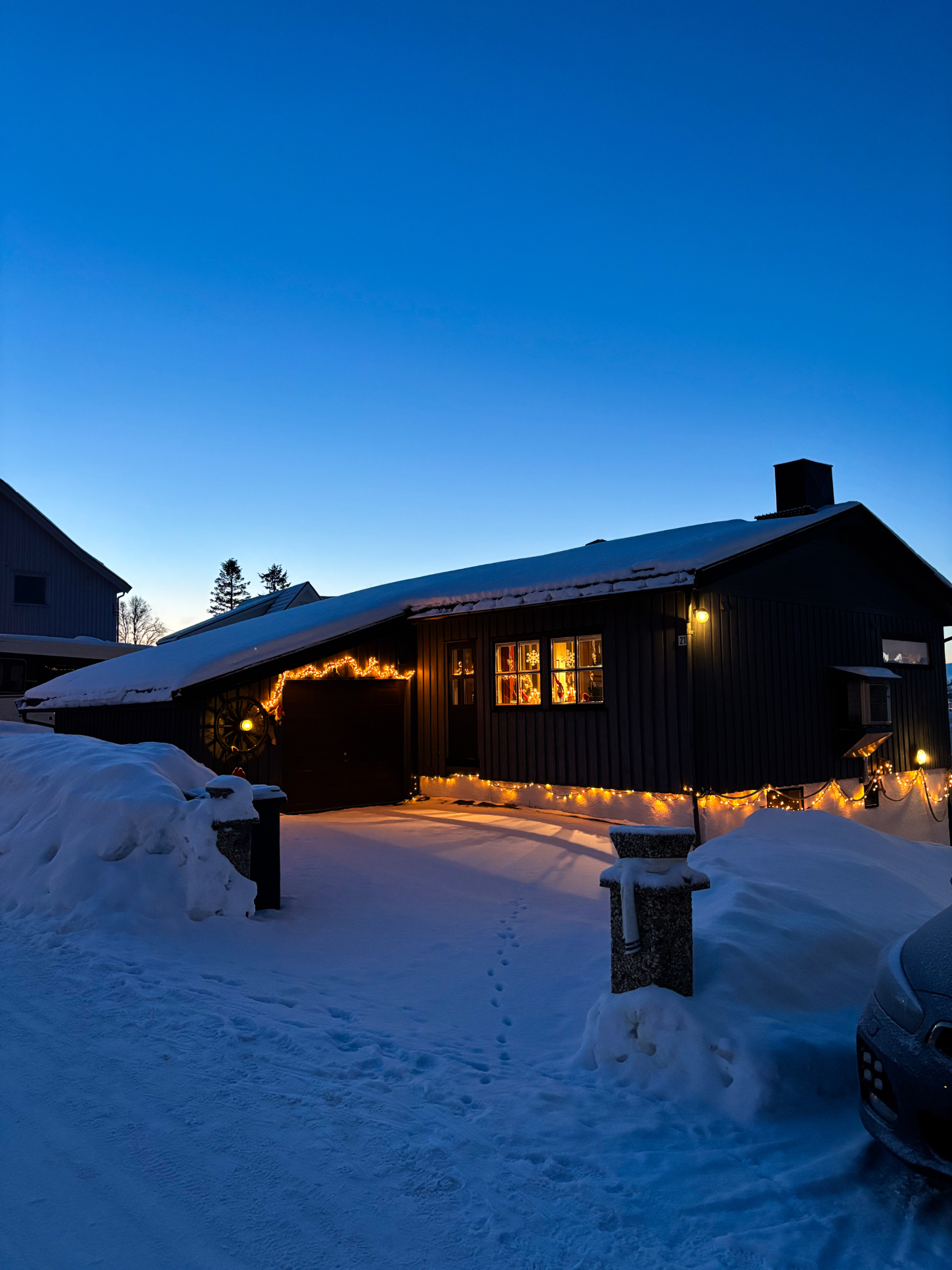 Maison en bois sombre de Tromsdalen décorée de guirlandes lumineuses dans la neige