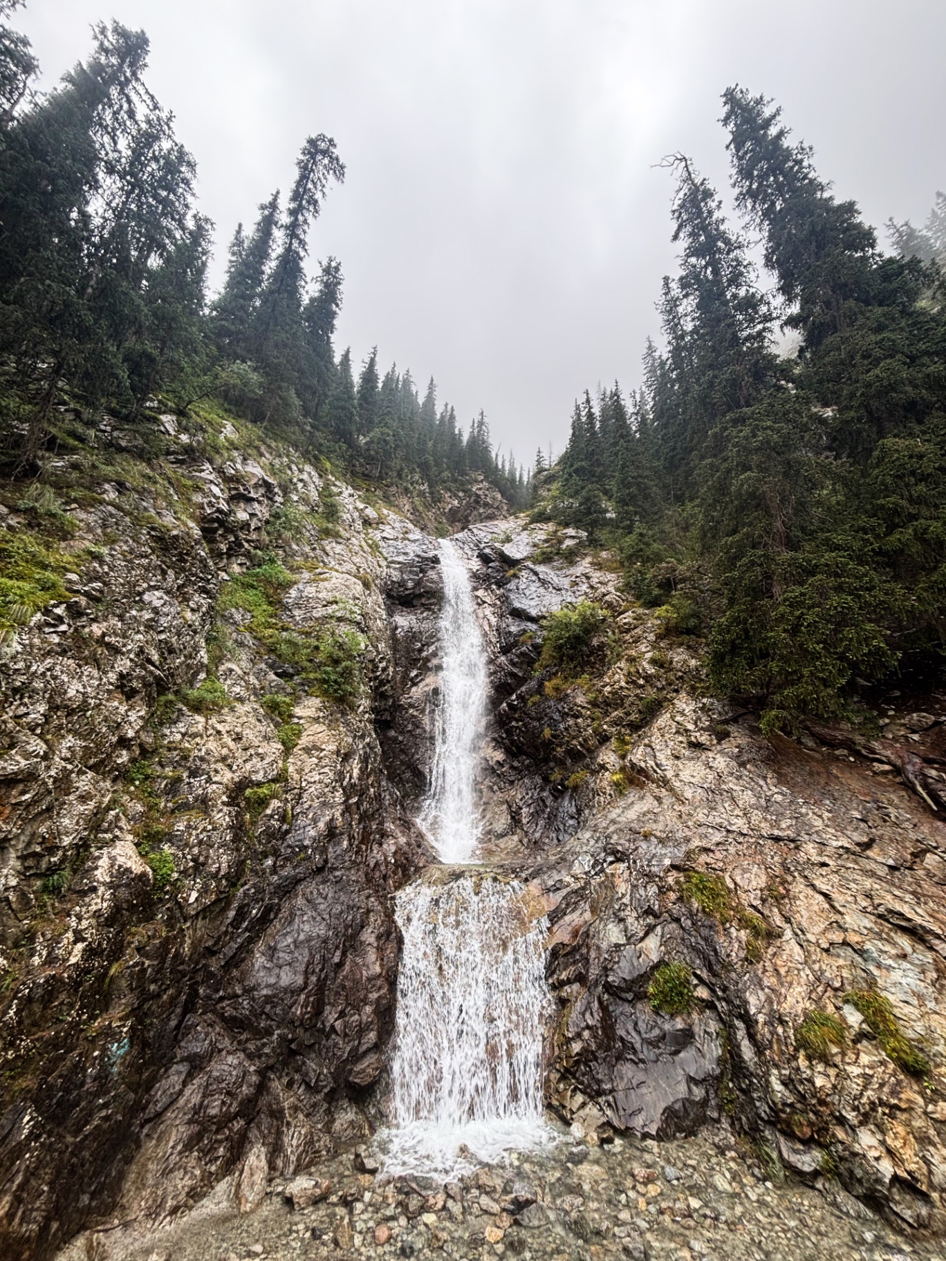 Cascade à deux paliers dévalant une paroi rocheuse dans la brume