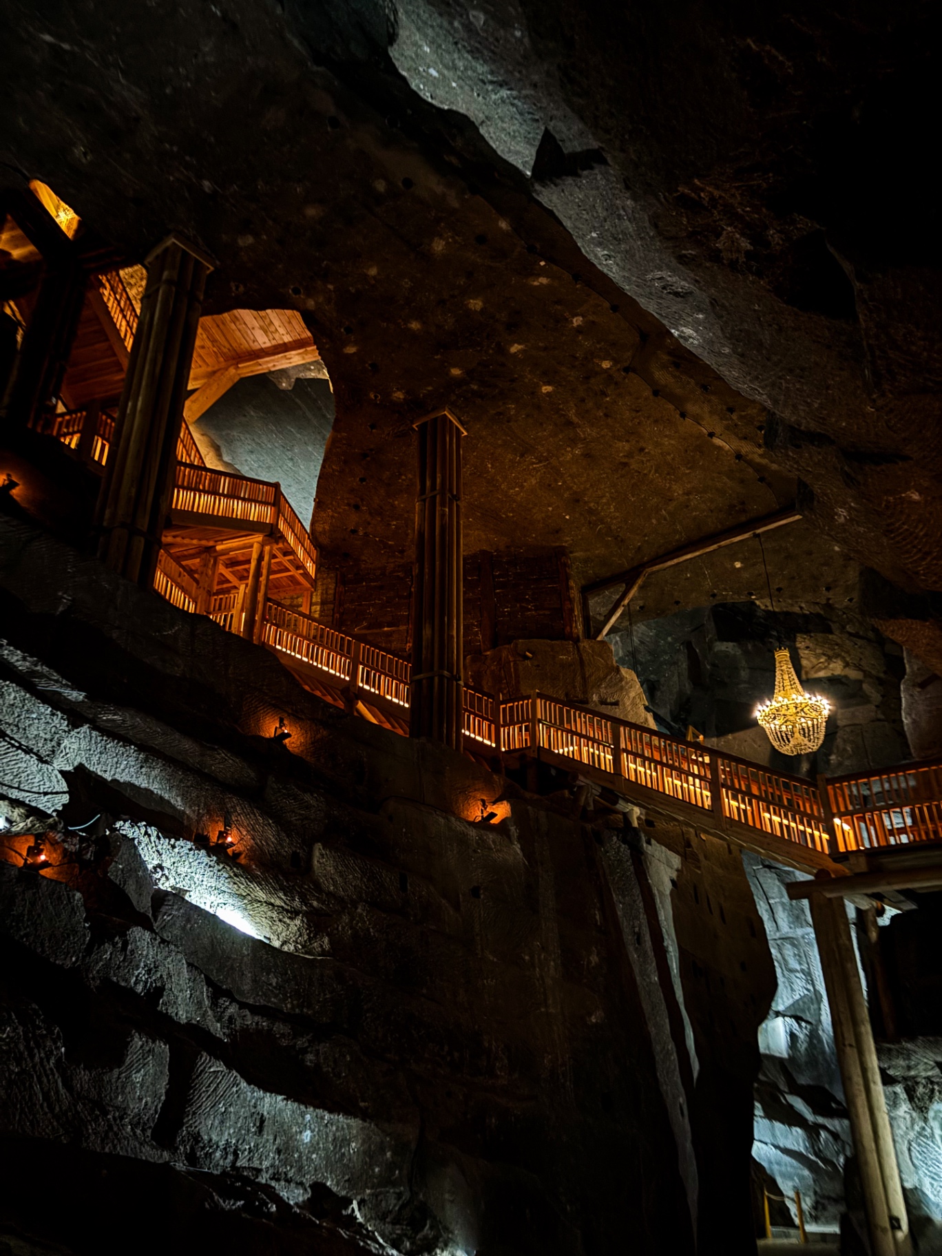 Galeries et escaliers de bois dominant une vaste salle de la mine, avec un lustre suspendu