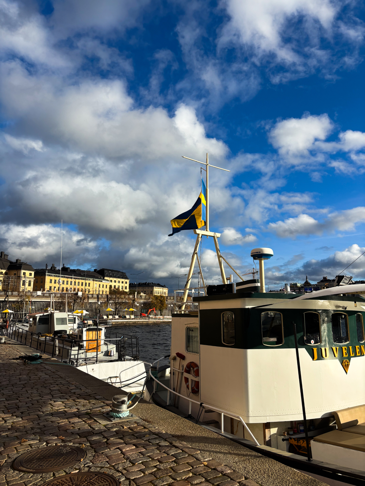 Petit bateau blanc amarré le long d’un quai pavé avec un drapeau suédois au vent