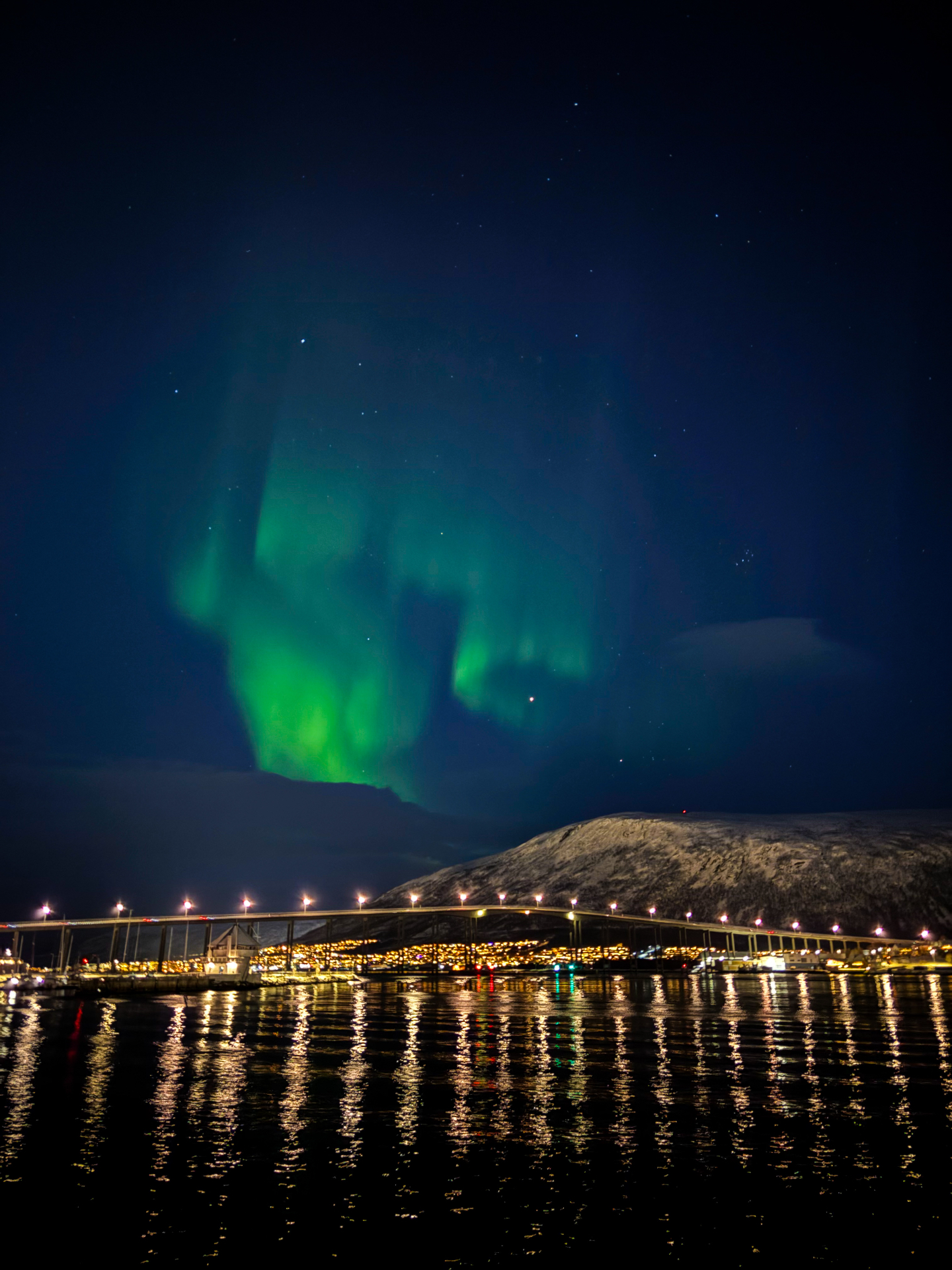 Aurore boréale verte au-dessus du pont de Tromsø, reflets dorés sur l’eau nocturne